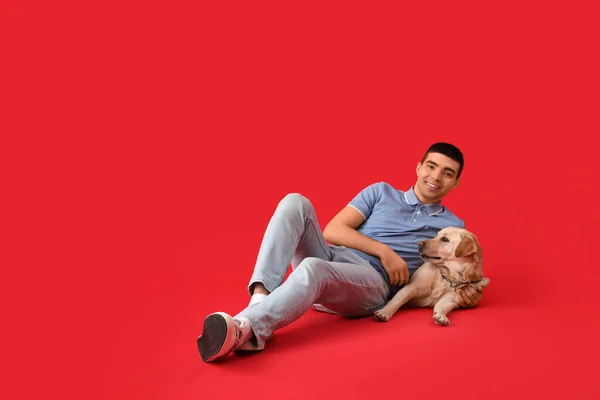年轻男子与可爱的拉布拉多犬躺在红色背景上 — 图库照片