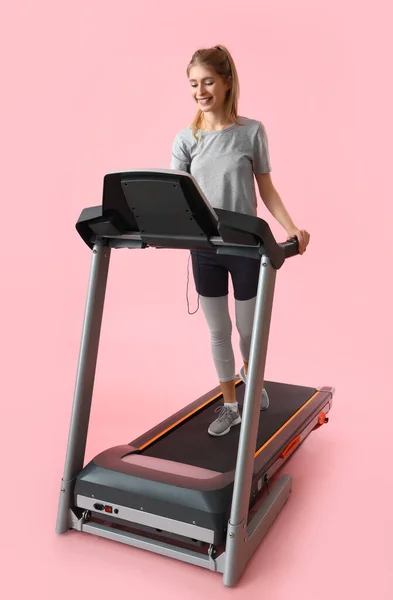 在粉红背景下的跑步机上训练的体态健壮的年轻女子 — 图库照片