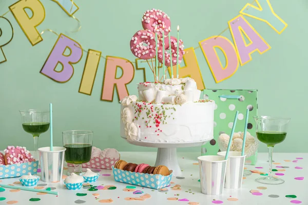 緑の壁の近くのテーブルの上に異なるお菓子と誕生日ケーキ — ストック写真