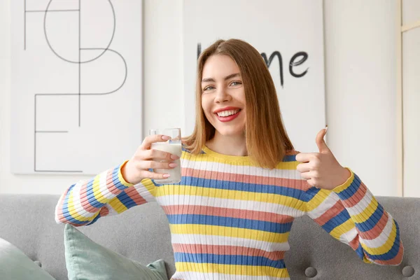 自宅で親指を示すミルクのガラスを持つ若い女性 — ストック写真
