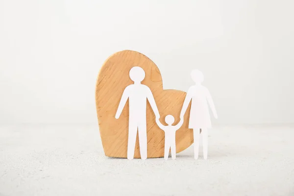 Wooden heart with figures of family on white table. Family love concept