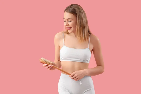 Young woman with anti-cellulite brush on pink background