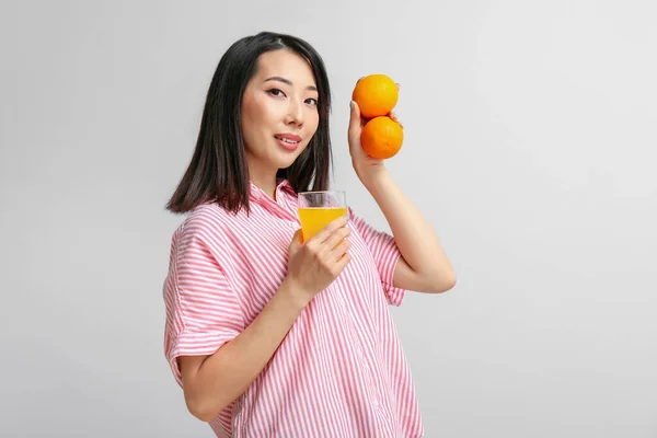 光の背景にオレンジとジュースのガラスが付いている美しいアジアの女性 — ストック写真