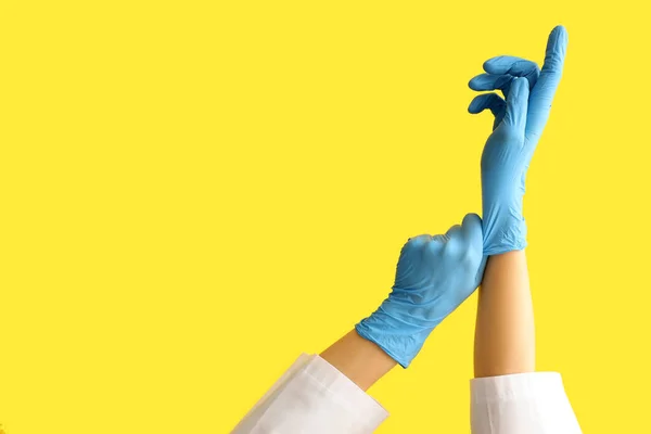 Vrouwelijke Arts Zet Medische Handschoenen Tegen Gele Achtergrond — Stockfoto