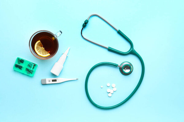 Stethoscope, pills, cup of tea and thermometer on blue background