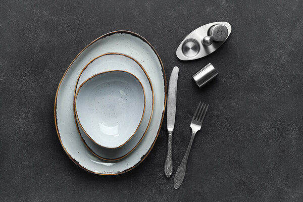 Clean plates, cutlery and salt shaker on black table