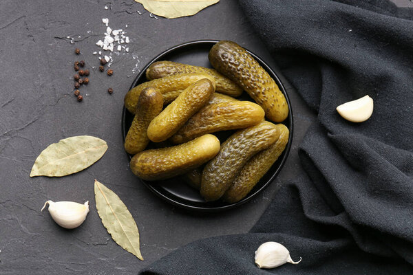 Plate with pickled cucumbers and different spices on black background