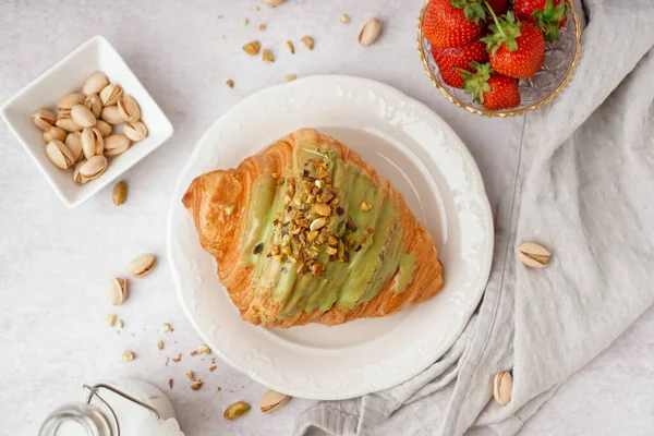 Plate with sweet croissant and pistachio nuts on white background