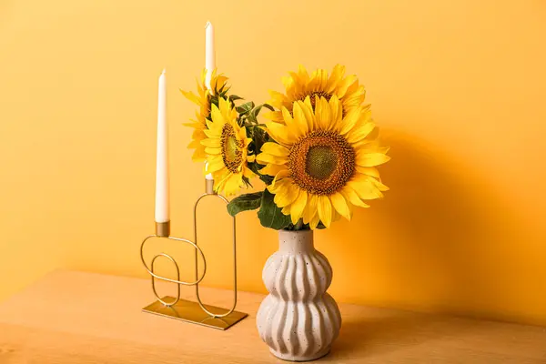 Vase with beautiful sunflowers and candles on table near orange wall in room, closeup