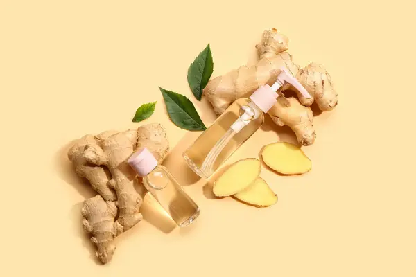Bottles of ginger cosmetic oil and leaves on yellow background