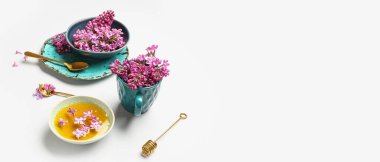 Beyaz arkaplanda seramik sofra takımı ve eflatun çiçekli bal kasesi