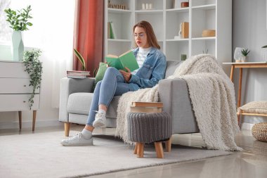 Evdeki kanepede kitap okuyan genç bir kadın.