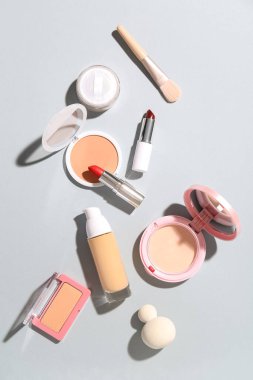Gri arkaplanda makyaj fırçası ve süngerli dekoratif kozmetik ürünler
