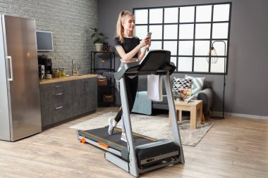 Spor genç bayan evdeki koşu bandında cep telefonu kullanıyor.