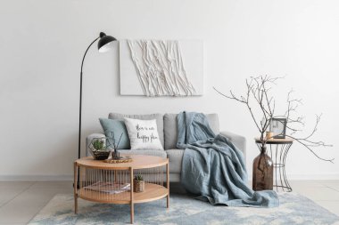 Beyaz duvarın yanında gri kanepesi ve kahve masası olan rahat bir oturma odası.