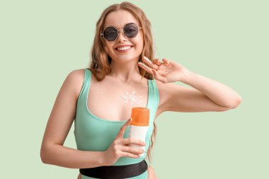 Yeşil arka planda güneş kremi sürmüş güzel genç bir kadın.