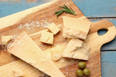 Mavi ahşap arka planda lezzetli parmesan peyniri parçaları olan tahta, yakın plan.