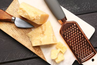 Koyu ahşap arka planda lezzetli parmesan peyniri parçaları olan tahta, yakın plan.