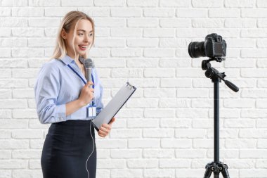 Beyaz tuğla arka planda mikrofon ve pano kayıt videosu olan kadın gazeteci