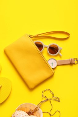 Saati olan şık bir çanta ve sarı arka planda farklı aksesuarlar.