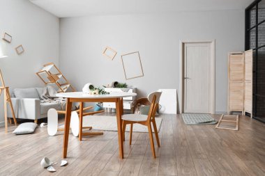 Düşmüş vazo ve çiçekli yemek masası dağınık bir odada.