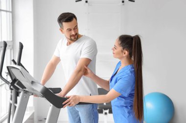 Rehabilitasyon merkezinde koşu bandında genç bir adamla çalışan kadın fizyoterapist.
