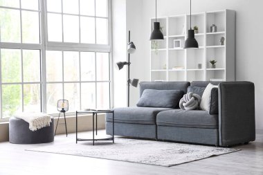 Büyük pencerenin yanında rahat gri kanepe ve sehpası olan aydınlık oturma odasının içinde.