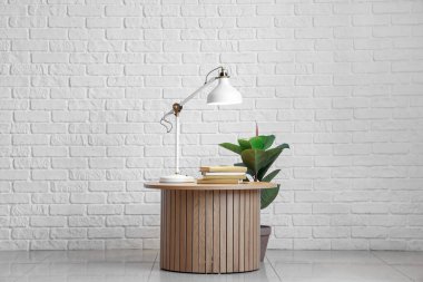 Parlayan lamba, kitaplar ve beyaz tuğla duvarın yanındaki çiçekli masa.