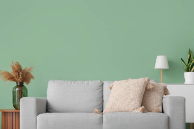 Oturma odasının içinde, yeşil duvarın yanında kanepe var.