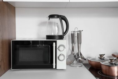 Mikrodalga fırını ve elektrikli su ısıtıcısı olan beyaz mutfak tezgahı.