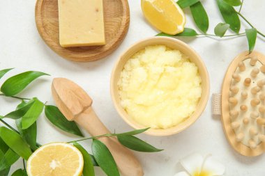 Bowl of lemon body scrub with massage brush, juicer and soap on white background