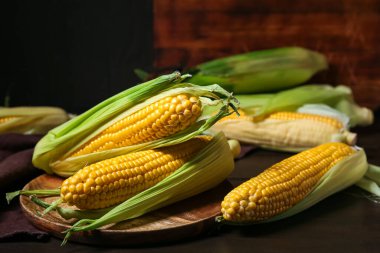 Plate with fresh corn cobs on black wooden table