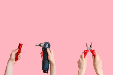 Electrician hands with tools on pink background