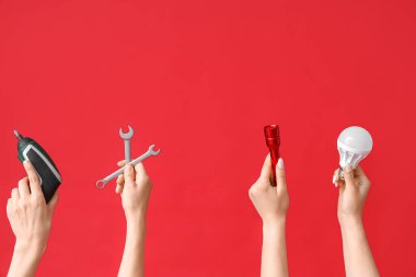 Electrician hands with tools and light bulb on red background