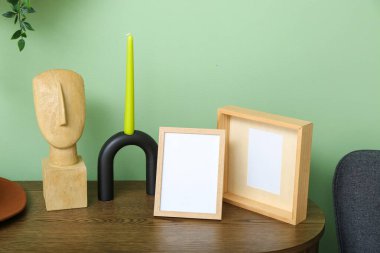 Odadaki yeşil duvarın yanındaki rafta mum ve dekor bulunan boş çerçeveler.