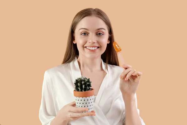 Pretty young woman with sugaring paste and cactus on beige background