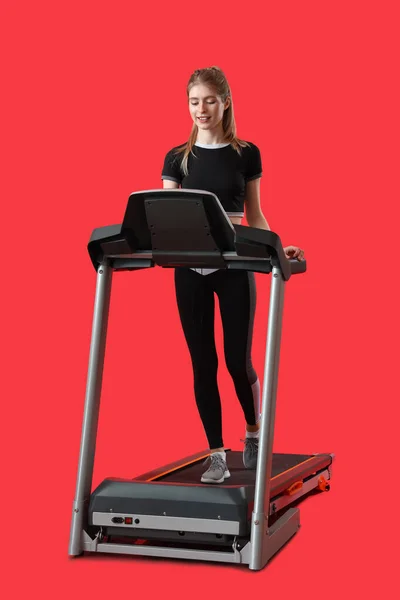 赤い背景に対してトレッドミルでスポーティな若い女性のトレーニング — ストック写真