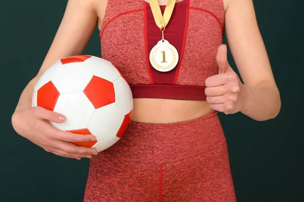 グリーンバックグラウンドで親指を示すメダルとボールを持つ女性サッカー選手 クローズアップ — ストック写真