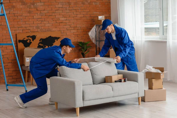 stock image Male movers wrapping sofa with stretch film in room