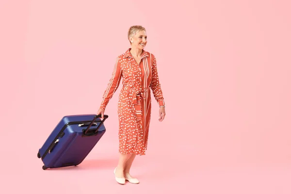 stock image Mature woman with suitcase on pink background