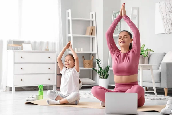 Working mother with her little daughter doing yoga at home