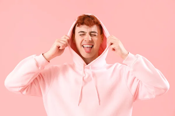 ピンクの背景に舌を示すフーディーの若い赤毛の男 — ストック写真