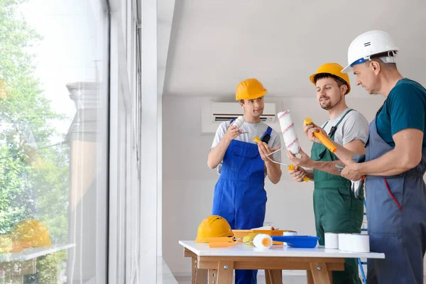带油漆滚筒的男性建筑工人小组在房间里工作 — 图库照片