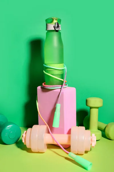 Set of sports equipment with bottle of water on green background
