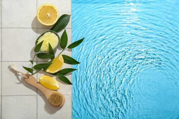 Lemon body scrub with plant branch and massage brush on edge of swimming pool
