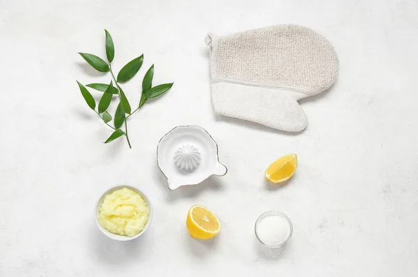 Bowl of lemon body scrub with massage glove and juicer on white background