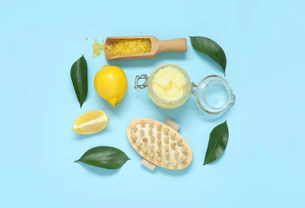 Jar of lemon body scrub with massage brush and sea salt on blue background