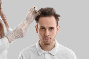 Gri arka planda saç büyümesi için serumu olan genç adam ve doktor.