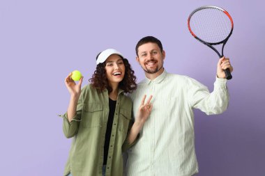 Genç bir çift tenis raketi ve leylak arkaplanda top oynuyorlar.