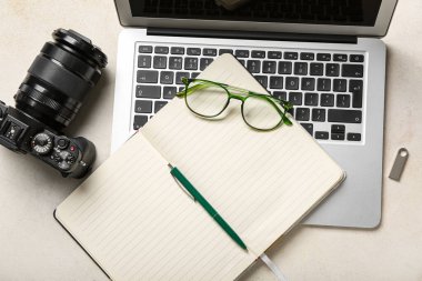 Gözlüklü, dizüstü bilgisayarlı ve beyaz arkaplanda fotoğraf makinesi olan bir defter.